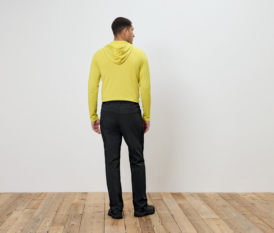 Un homme portant un sweat à capuche jaune et un pantalon noir se tient dos à la caméra.