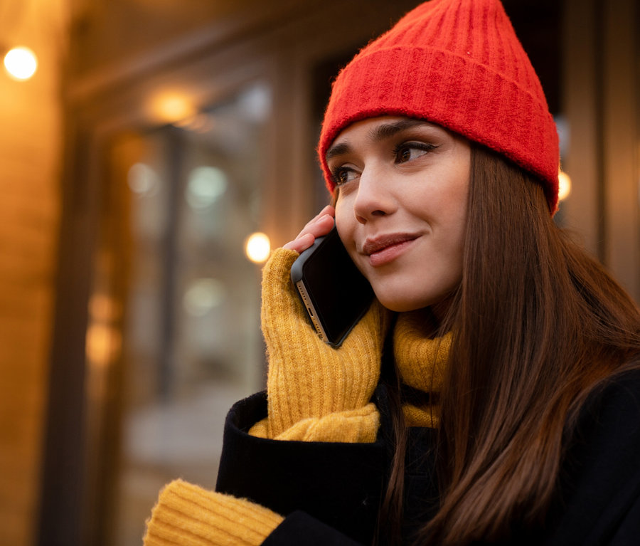 Femme avec bonnet rouge et gants jaunes téléphonant.