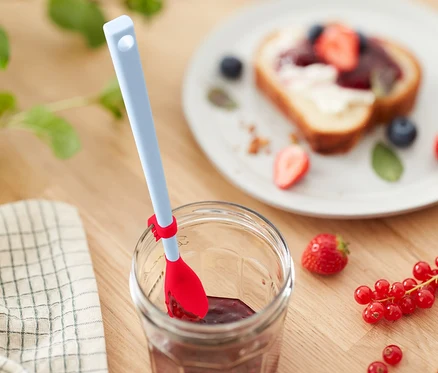Cuillère en silicone spéciale dans un pot de confiture à côté d'un pain aux fruits.