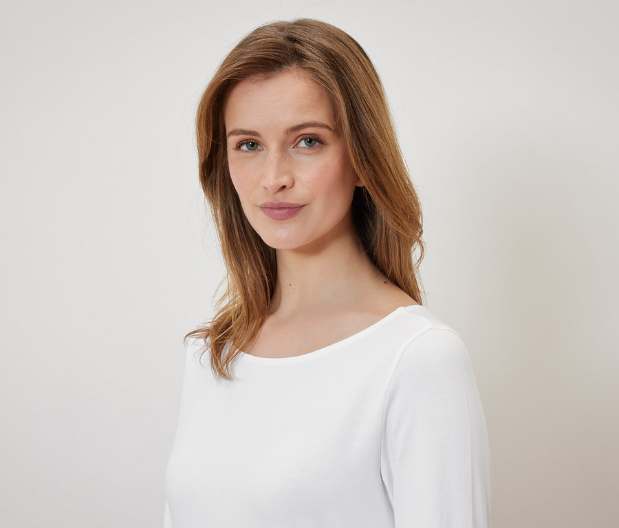 Portrait d'une femme aux cheveux bruns et aux yeux bleus portant un t-shirt blanc.
