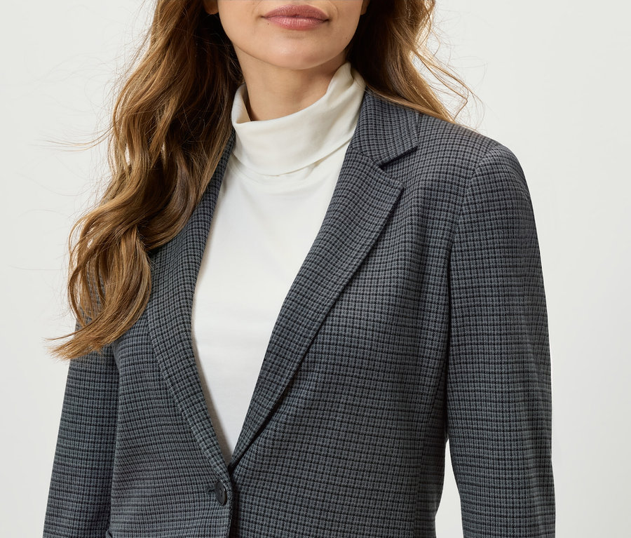 Une femme porte un blazer à carreaux et un col roulé blanc.