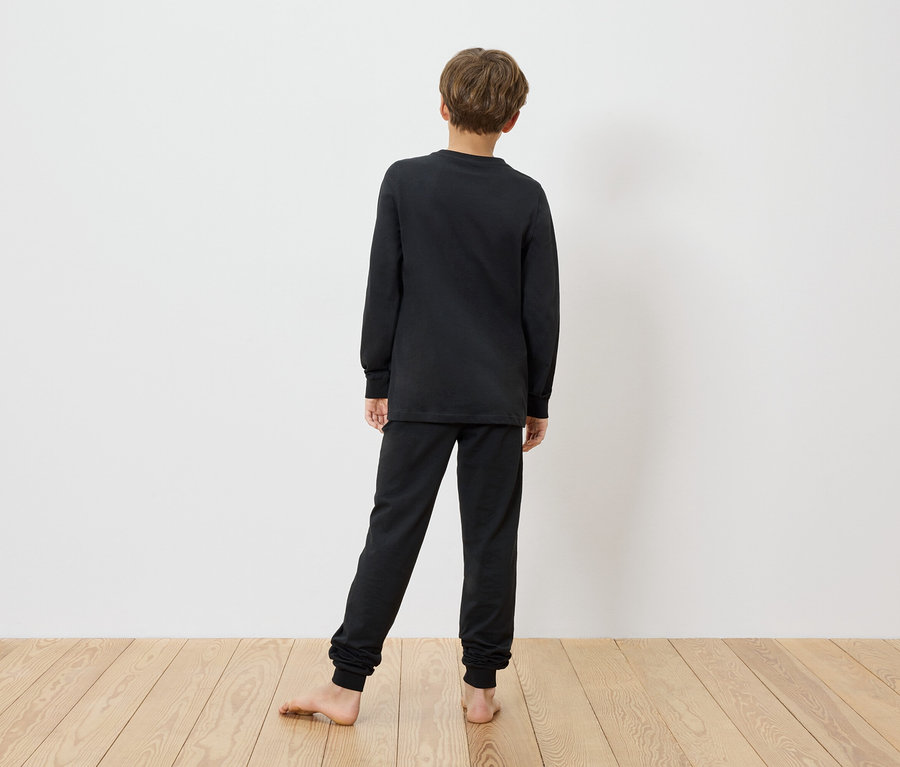Un enfant se tient pieds nus devant un mur blanc et porte un pyjama noir pour enfant MINECRAFT.