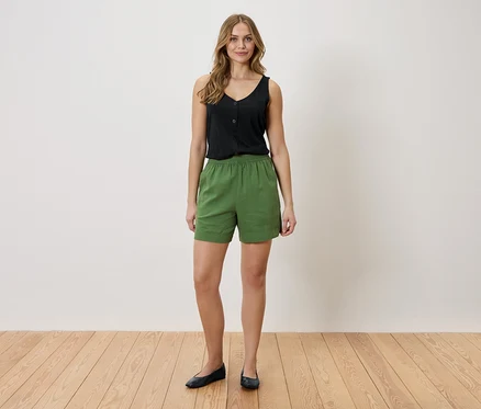Une femme se tient devant un mur blanc. Elle porte un haut noir et un short vert.