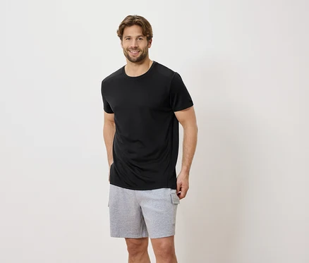 Homme portant un t-shirt noir et un short gris devant un fond blanc.