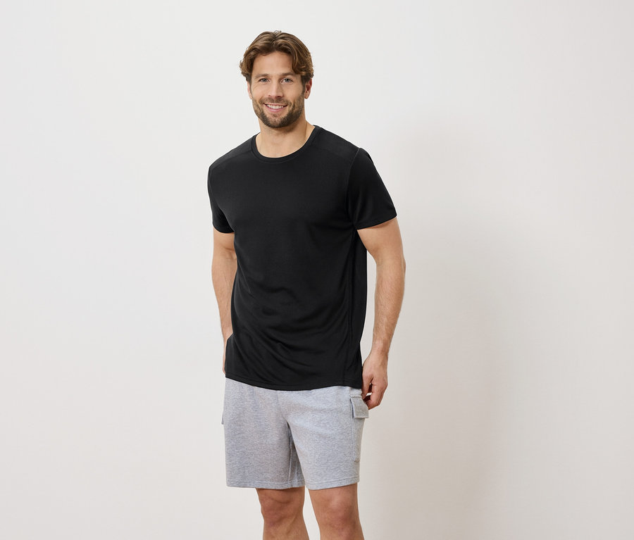 Homme portant un t-shirt noir et un short gris devant un fond blanc.