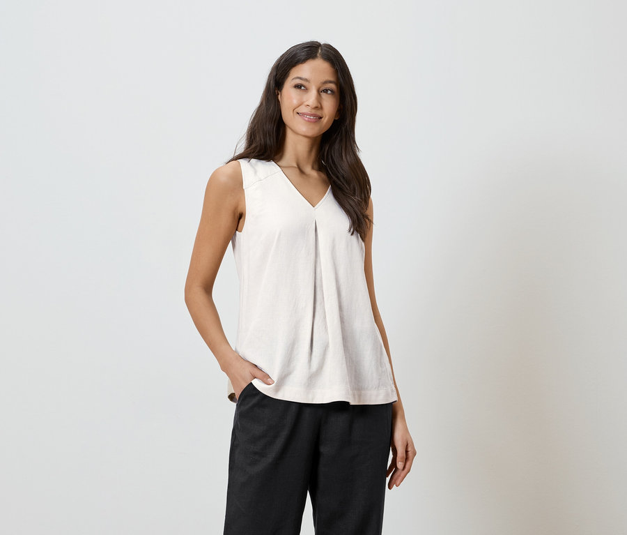 Une femme aux cheveux foncés porte un haut clair et un pantalon foncé, avec une main dans sa poche.