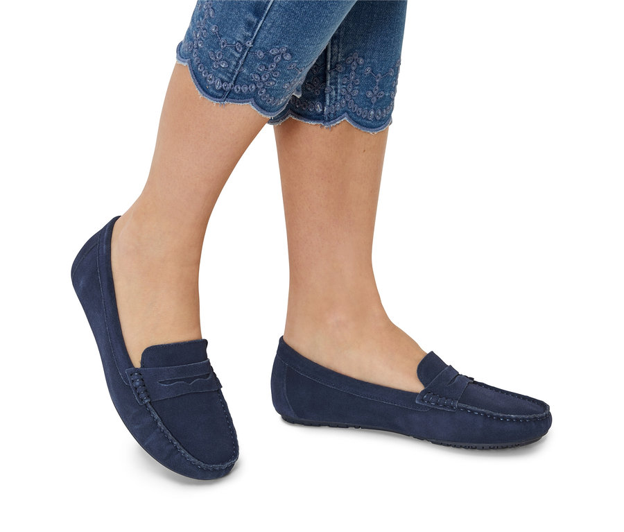 Gros plan de jambes portant un jean brodé et des mocassins en daim bleu.