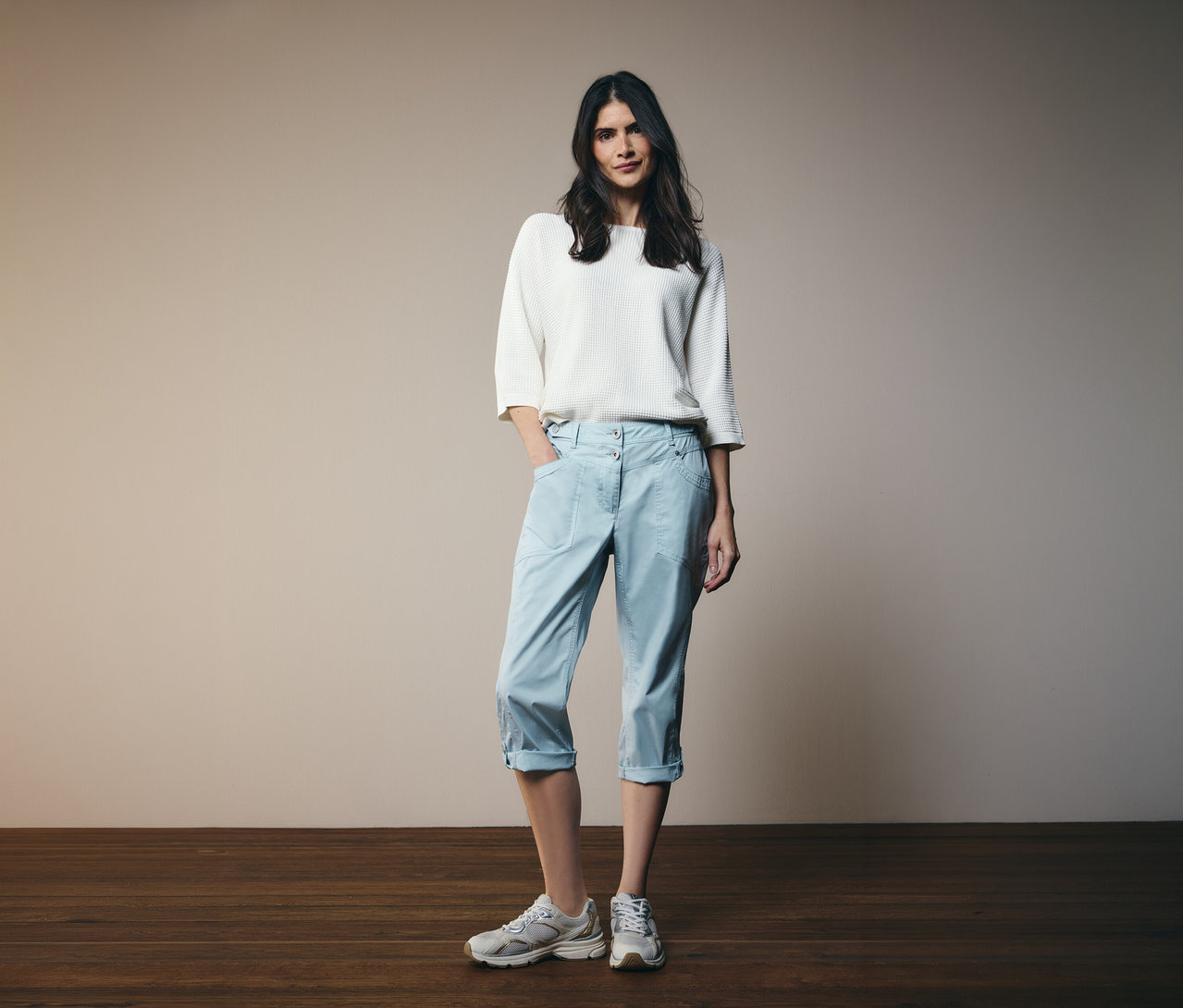 Femme portant un haut blanc et un pantalon 3/4 Cecil «
New York
» bleu clair. Une main dans la poche.