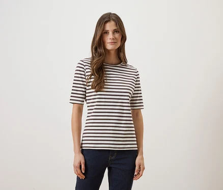 Une femme aux longs cheveux bruns portant un t-shirt rayé et un jean sur un fond blanc.
