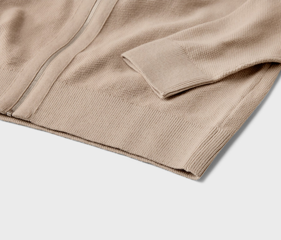 Gros plan d'un cardigan beige en tricot avec fermeture éclair et poignets côtelés.