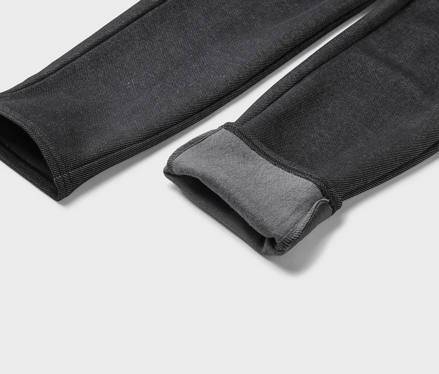 Gros plan sur deux jambes de pantalon noires avec une doublure en polaire grise à l'ourlet sur fond blanc.