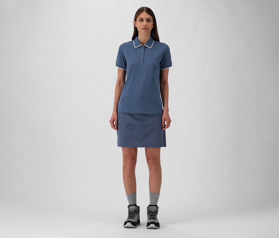 Femme portant un polo bleu CMP en piqué stretch et une jupe avec des chaussettes grises et des chaussures de randonnée.