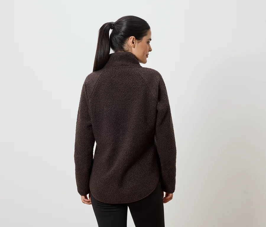 Vue arrière d'une femme portant un pull en polaire marron et un pantalon noir, les cheveux attachés en queue de cheval, sur fond blanc.