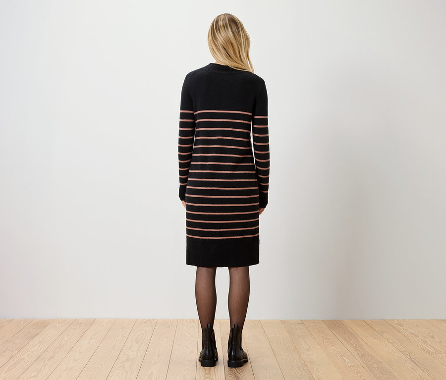 Vue arrière d'une femme aux cheveux blonds portant une robe rayée arrivant aux genoux, des collants noirs et des bottines.