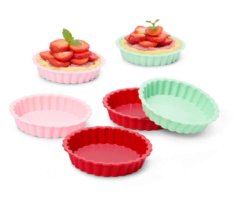 Plusieurs moules à tarte colorés, certains remplis de tartelettes aux fraises.