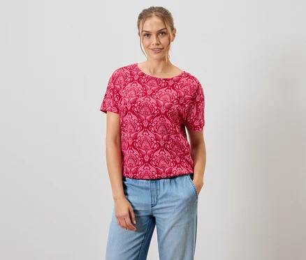 Femme portant un t-shirt rouge à motifs et un jean bleu.