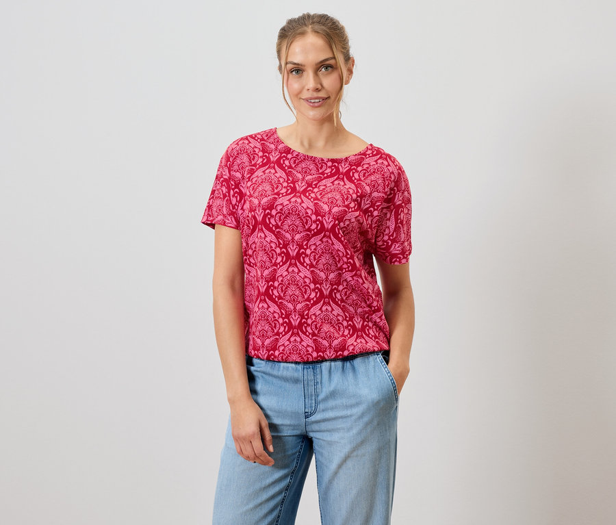 Femme portant un t-shirt rouge à motifs et un jean bleu.