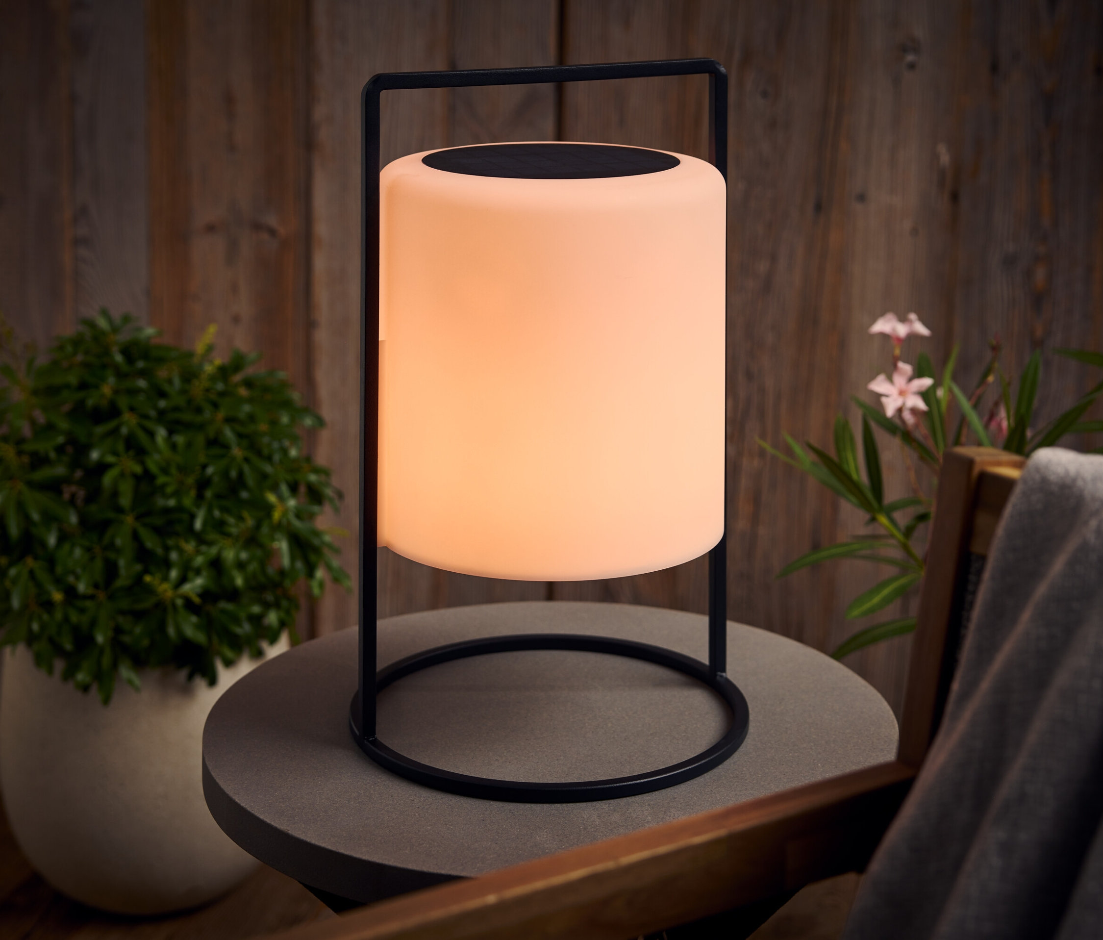 Une lampe lumineuse avec un cadre noir se dresse sur une table grise à l'extérieur.