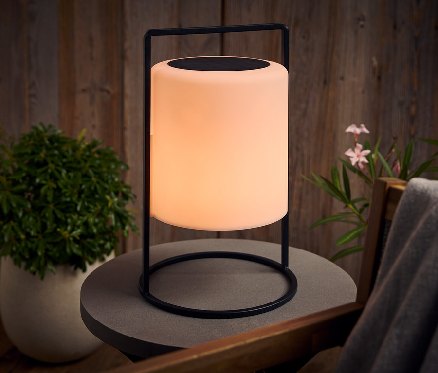 Une lampe lumineuse avec un cadre noir se dresse sur une table grise à l'extérieur.