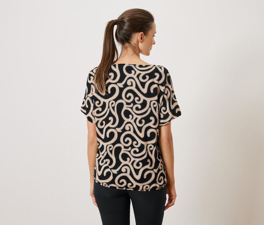 Vue arrière d'une femme avec une queue de cheval portant un chemisier à motifs noir et beige et un pantalon noir.