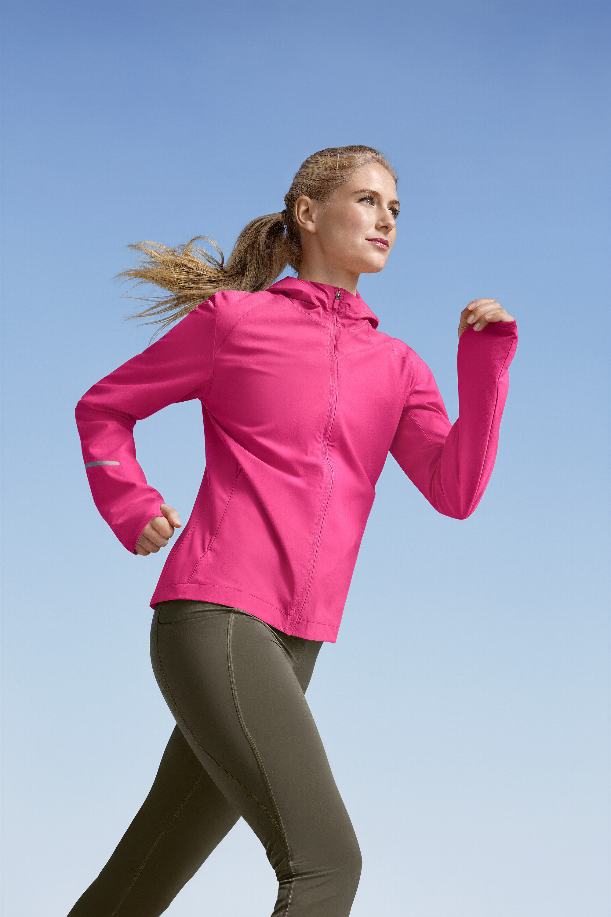 Femme courant en veste de course rose et leggings de sport verts »ActivePower« sur fond de ciel bleu.