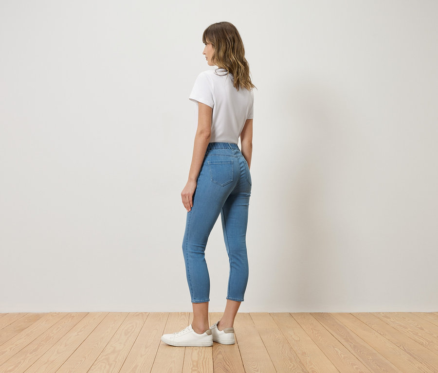 Femme vue de dos, portant un t-shirt blanc, un jean bleu et des baskets blanches.