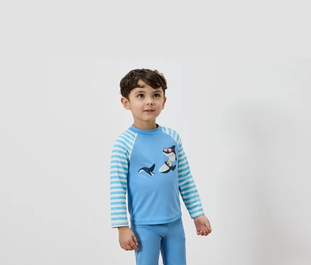 Un garçon porte un t-shirt à manches longues bleu clair avec un motif de requin et un pantalon bleu assorti.