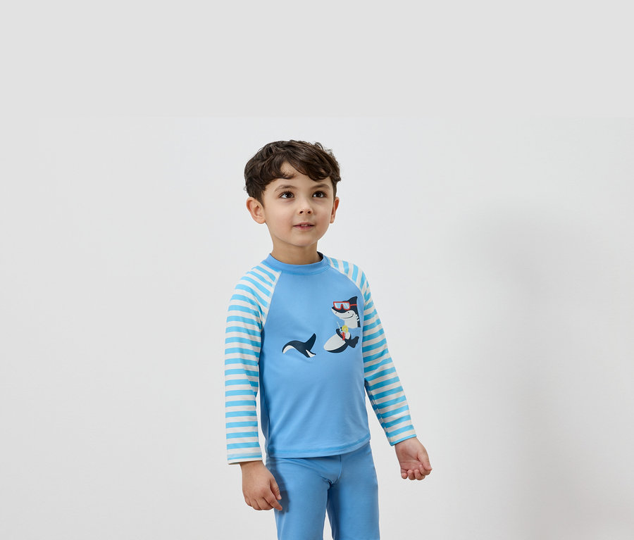 Un garçon porte un t-shirt à manches longues bleu clair avec un motif de requin et un pantalon bleu assorti.