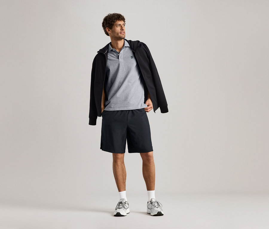 Homme portant une veste en sweat sur un polo gris avec un short.