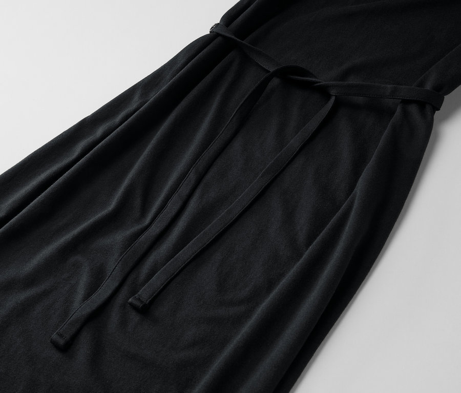 Gros plan d'une longue robe noire avec une ceinture à nouer sur un fond clair.