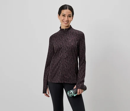 Une femme portant un legging noir et une veste marron à motifs tient une bouteille d'eau devant un fond gris.