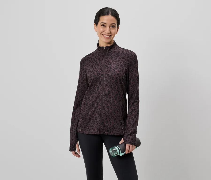 Une femme portant un legging noir et une veste marron à motifs tient une bouteille d'eau devant un fond gris.