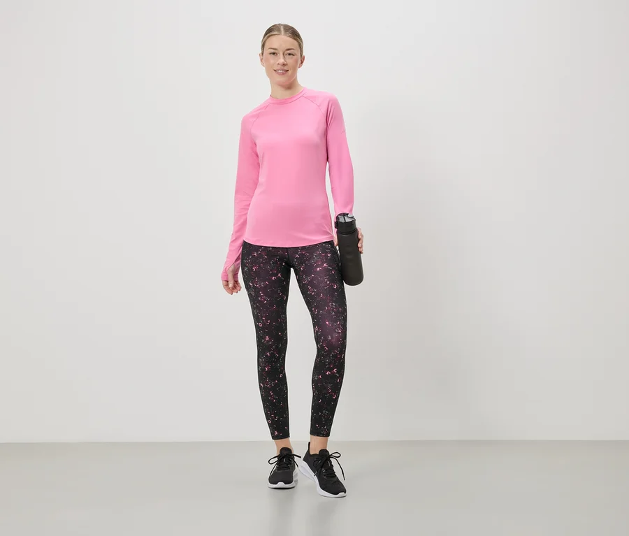 Une femme portant un haut rose à manches longues et un legging à fleurs tient une bouteille d'eau noire.