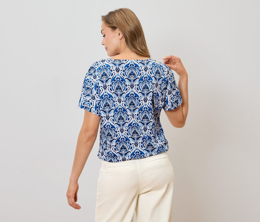 Vue arrière d'une femme blonde portant un chemisier à motifs bleus et blancs et un pantalon clair.