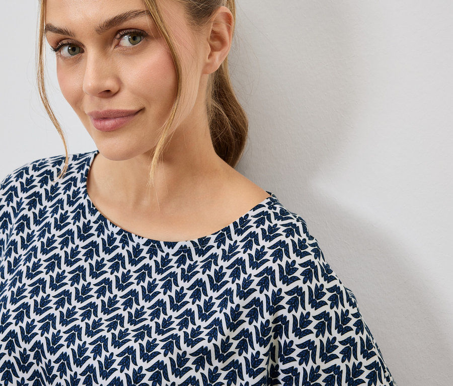 Portrait d'une femme blonde portant un haut bleu et blanc à motifs de feuilles.