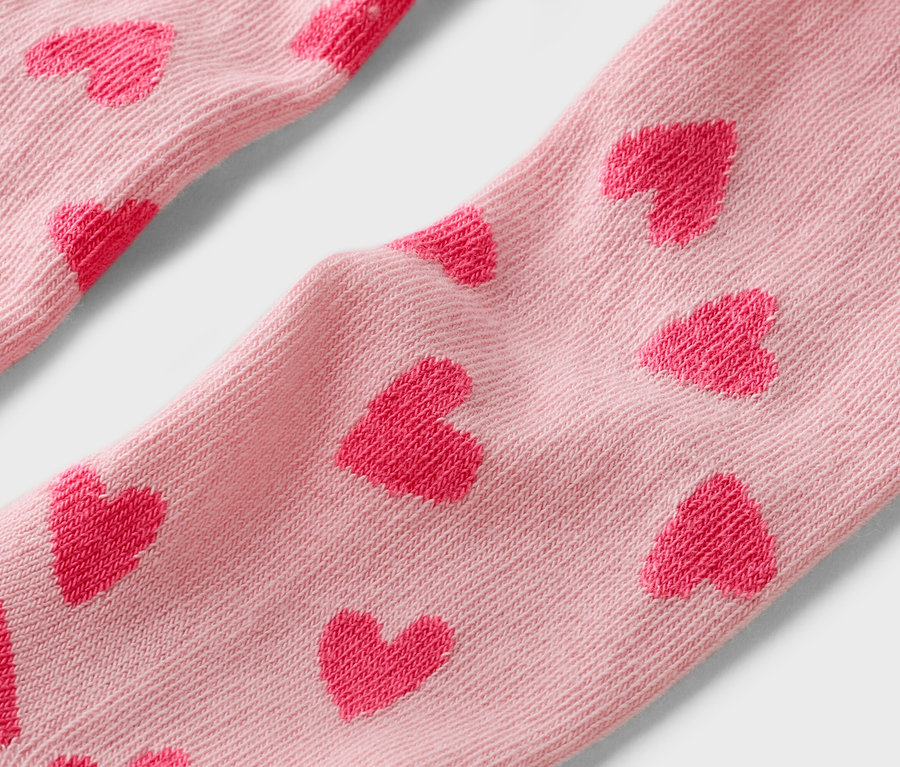 Gros plan de chaussettes rose clair avec un motif de petits cœurs rouges.