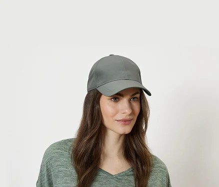 Femme portant une casquette de baseball verte et un haut vert sur fond blanc.