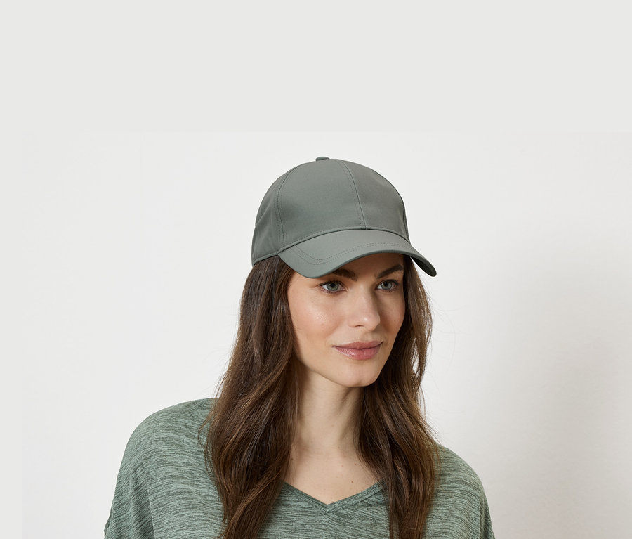 Femme portant une casquette de baseball verte et un haut vert sur fond blanc.