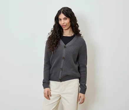 Femme portant un cardigan en tricot gris boutonné et un pantalon clair.