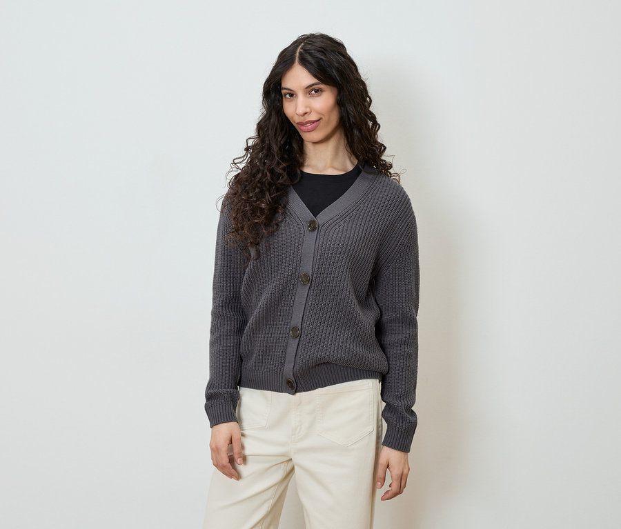 Femme portant un cardigan en tricot gris boutonné et un pantalon clair.