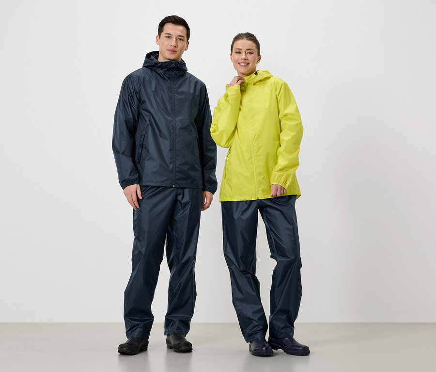 Un homme en veste et pantalon de pluie bleu marine se tient à côté d'une femme en veste de pluie jaune et pantalon de pluie bleu marine.