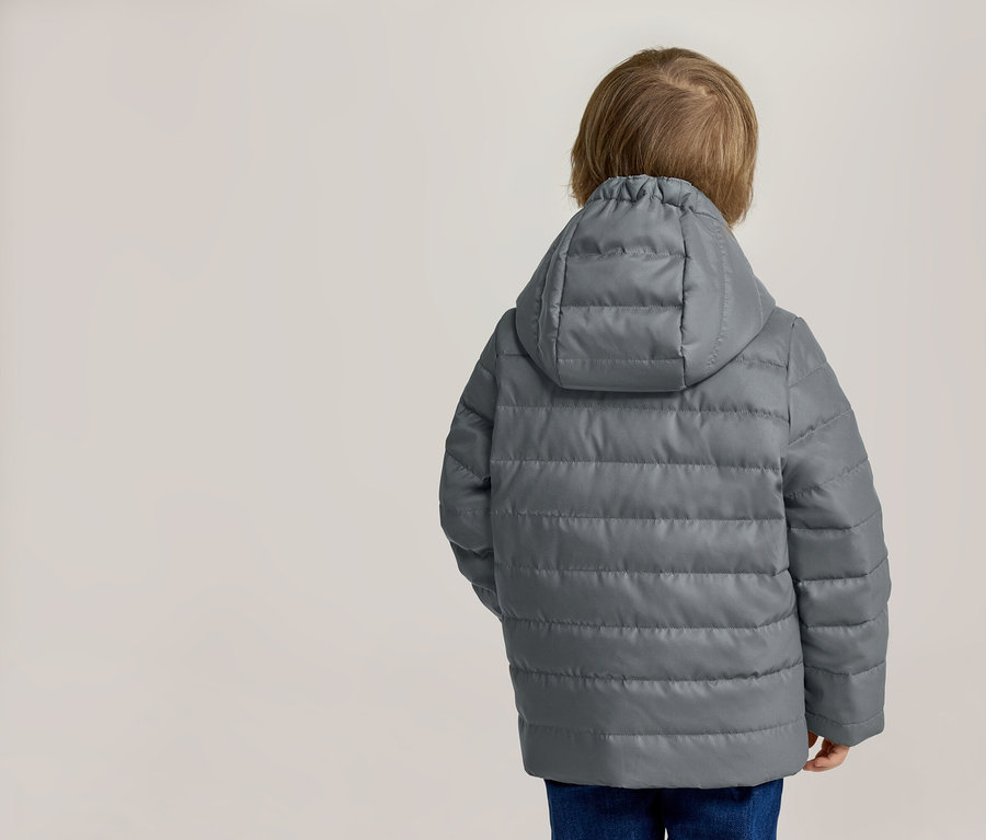 Vue arrière d'un enfant blond portant une veste matelassée grise à capuche et un jean bleu.