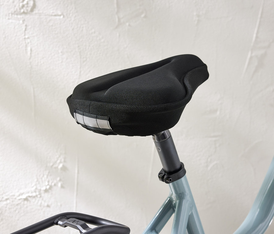 Gros plan d'une selle de vélo avec une housse noire et des bandes réfléchissantes sur un fond de mur blanc.