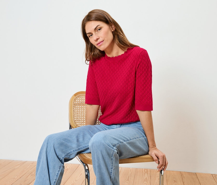 Une femme est assise sur une chaise, portant un haut rouge et un jean.