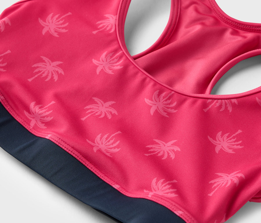 Gros plan d'un soutien-gorge de sport rose à motif de palmiers avec une bande marine.