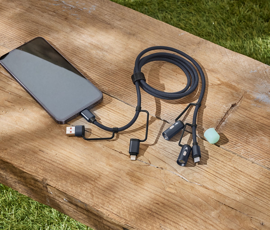 Un smartphone gris est connecté à un câble de charge multiple noir tressé sur un banc en bois.
