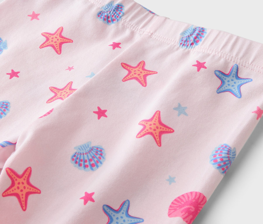 Gros plan sur des leggings rose clair avec une taille élastique, imprimés d'étoiles de mer orange, d'étoiles de mer bleues et de coquillages bleus et roses.