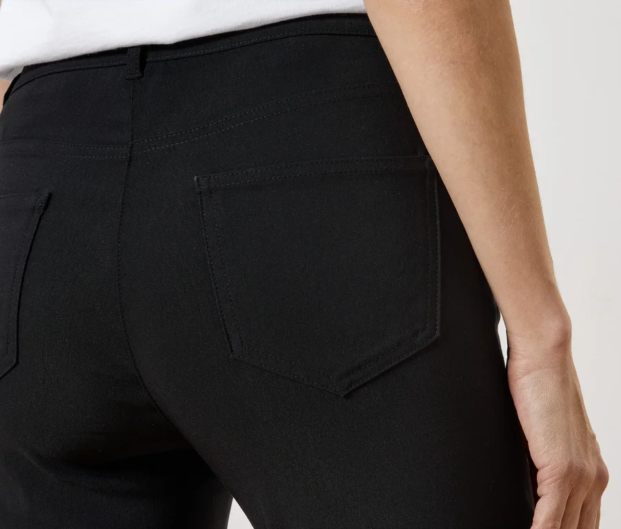 Vue arrière d'une personne portant un pantalon noir avec des poches arrière et un haut blanc.