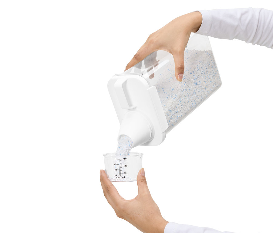 Une personne verse de la lessive d'un récipient transparent dans une tasse à mesurer.