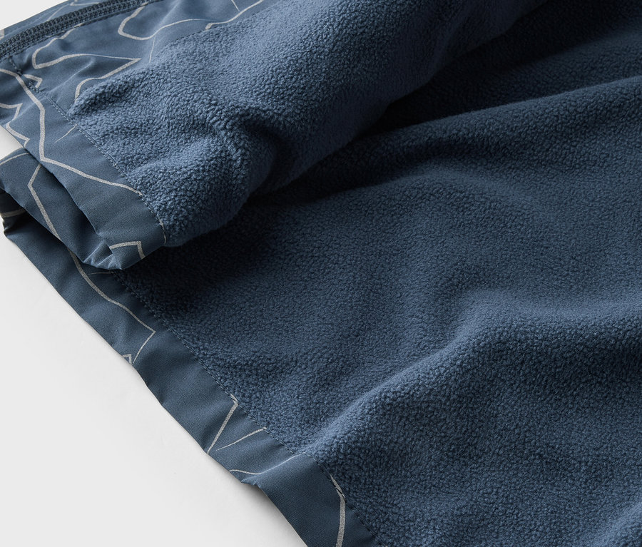Gros plan d'une couverture en polaire bleu marine avec un motif blanc, partiellement enroulée.